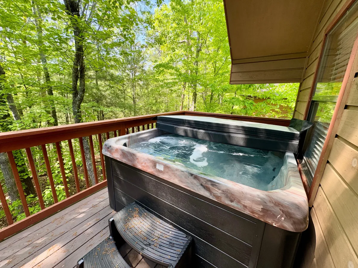 A tranquil exterior scene showing a hot tub nestled on a private deck surrounded by trees, inviting guests to soak and unwind in a peaceful natural setting.