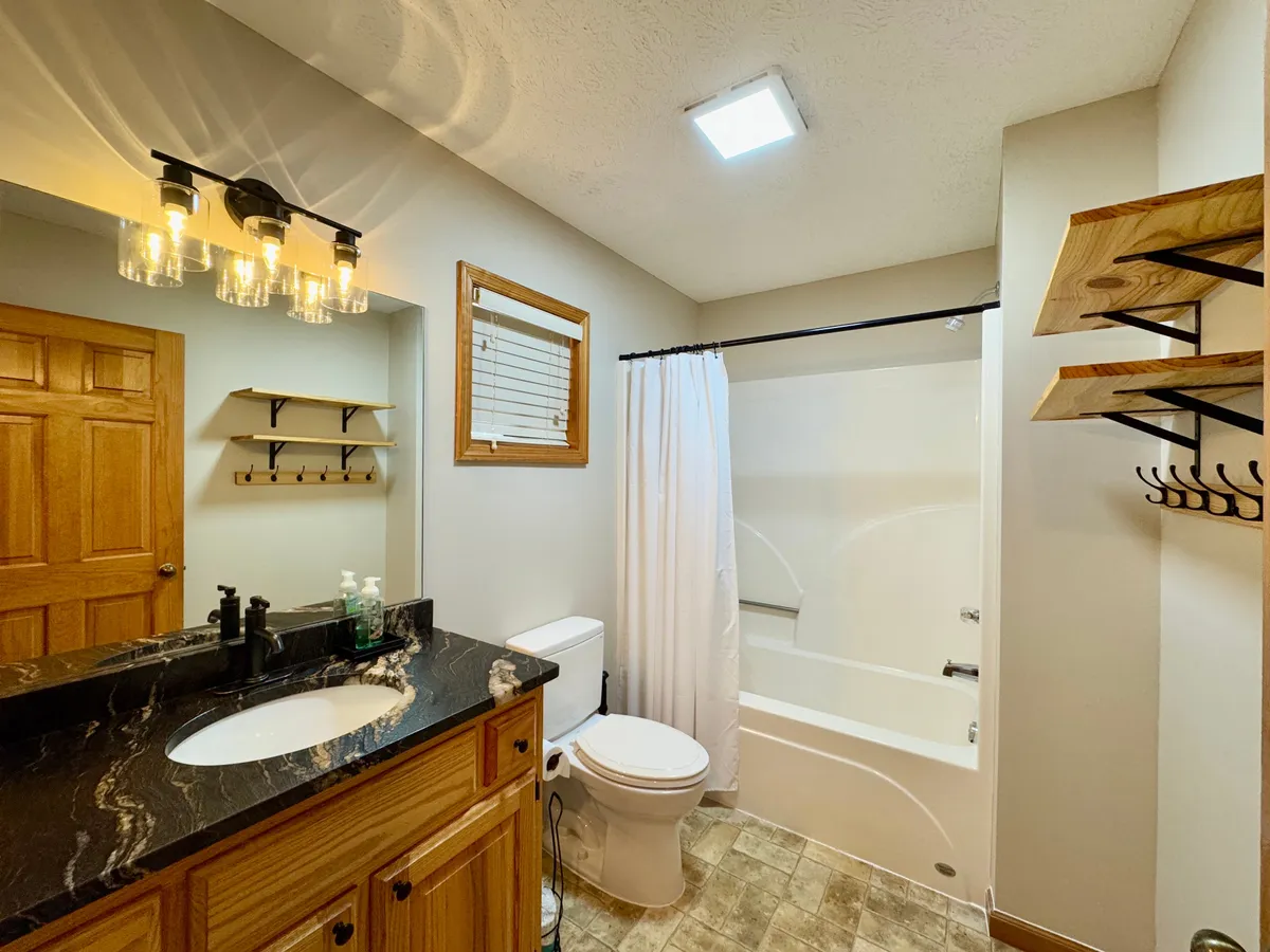 A bright and functional bathroom with a vanity and sink, a bathtub, wooden shelving for storage, and a mirror. The space is both inviting and practical, offering a spot for refreshing showers, soothing baths, and well-organized essentials.