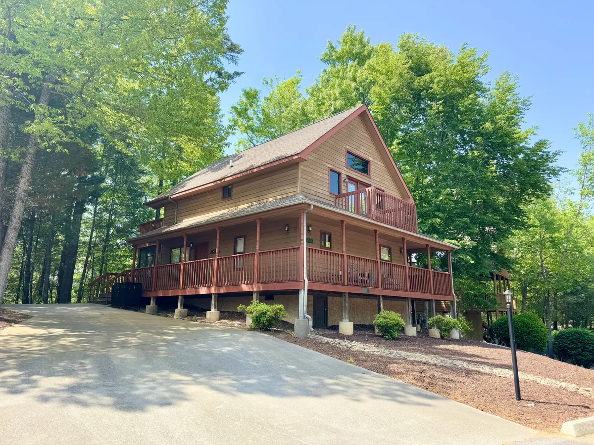 This exterior shot captures the wooden structure of the house, the expansive porch with railings, and lush greenery that frames the home. The scene suggests a seamless flow between indoor comfort and outdoor enjoyment.