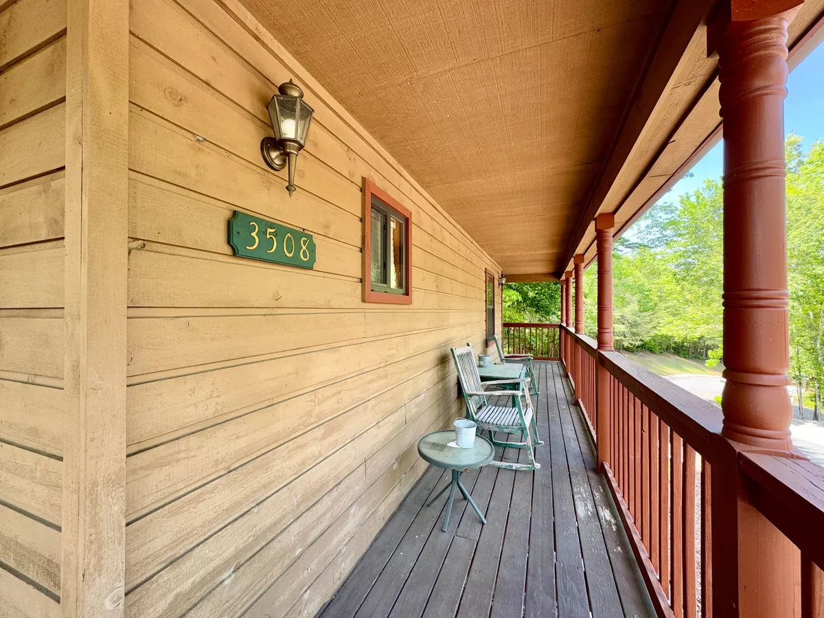 The image features a charming exterior porch with house number 3508, a vintage-style lamp, green chairs, and a small round table. Surrounded by greenery, it evokes a sense of arrival and relaxation, perfect for sipping coffee or socializing outdoors after a day of adventure.