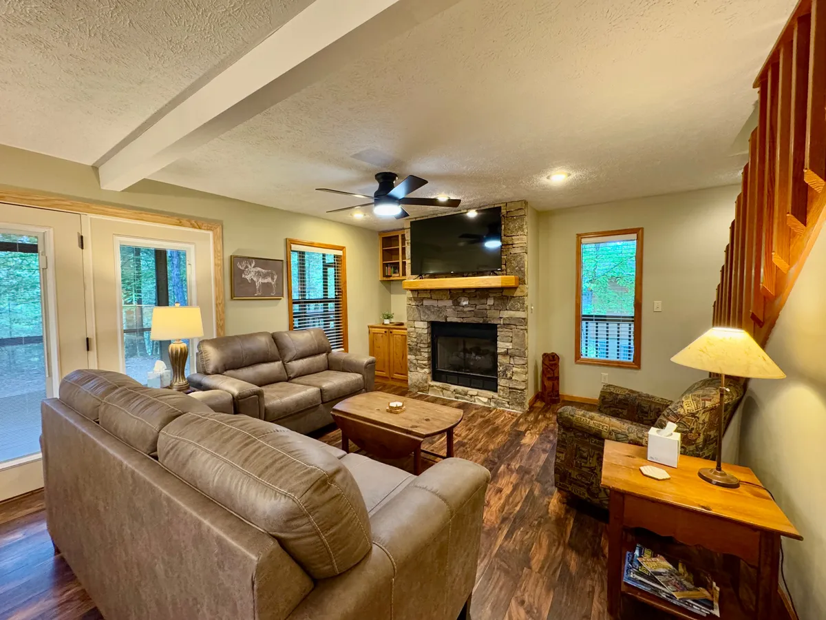Inside, a cozy living room features a stone fireplace, comfortable seating, a TV, and wooden furniture, making it a prime space for family movie nights or gathering to share stories after theme park adventures.