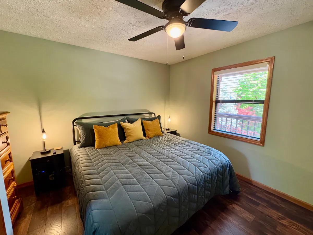 A cozy bedroom with a bed adorned with decorative pillows sits near a window that lets in abundant natural light. The nightstand with a lamp creates a welcoming ambiance, perfect for unwinding after a day of exploration. The scene conveys a peaceful, intimate retreat, ideal for couples seeking relaxation.