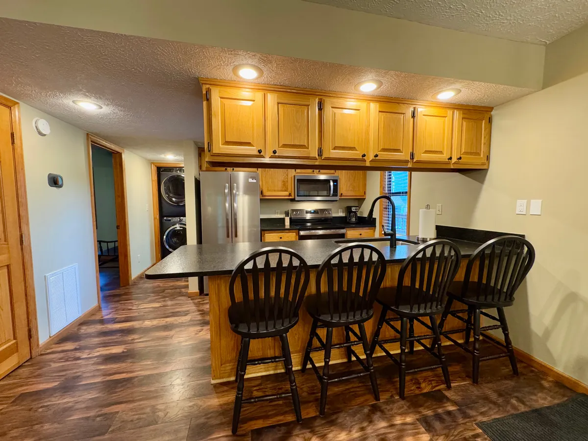 The kitchen is showcased with a central island, bar stools, stainless steel appliances, and wooden cabinetry. The space feels open, modern, and functional, inviting guests to gather for meal prep, casual dining, or shared recipes.
