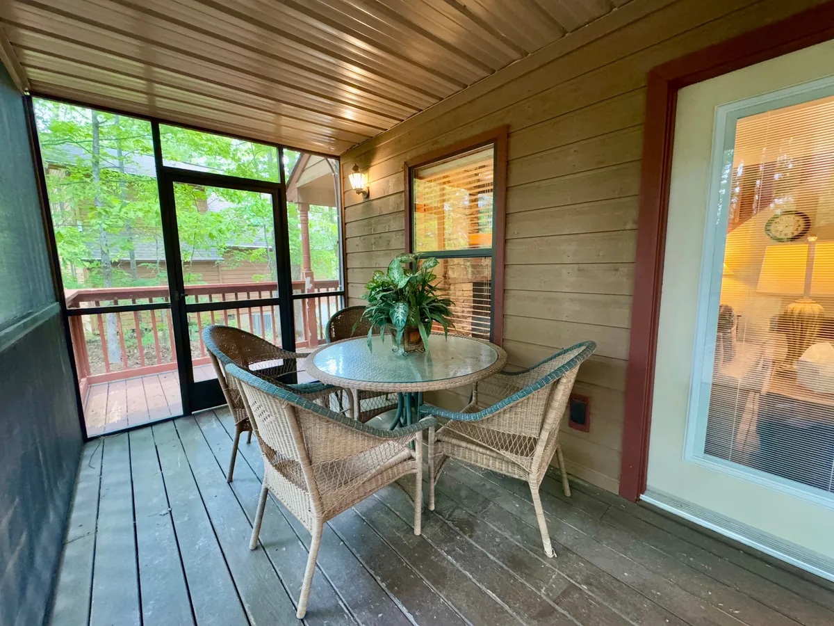 This image features a glass table surrounded by comfortable wicker chairs and a potted plant, all situated in a screened-in porch setting. The space is inviting and perfect for enjoying morning coffee or relaxing while being shielded from the outdoors.