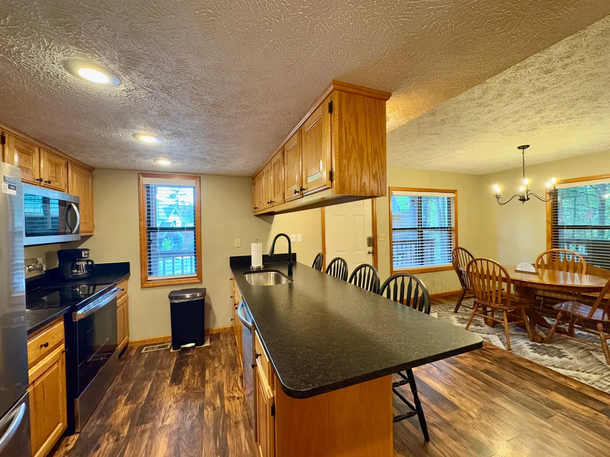 An open-concept kitchen and dining area with a central kitchen island, a spacious dining table, and a large window offering a glimpse of the surrounding scenery. The setup is ideal for communal meals and shared cooking experiences, reinforcing the idea of spending quality time together.