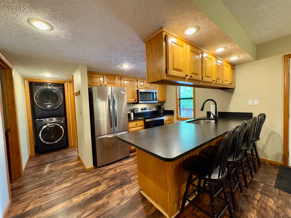 A modern kitchen highlighted by a substantial island, stainless steel appliances, and a washer-dryer unit. The layout is perfect for group meal prep, celebrations, and daily convenience, emphasizing functionality and togetherness.