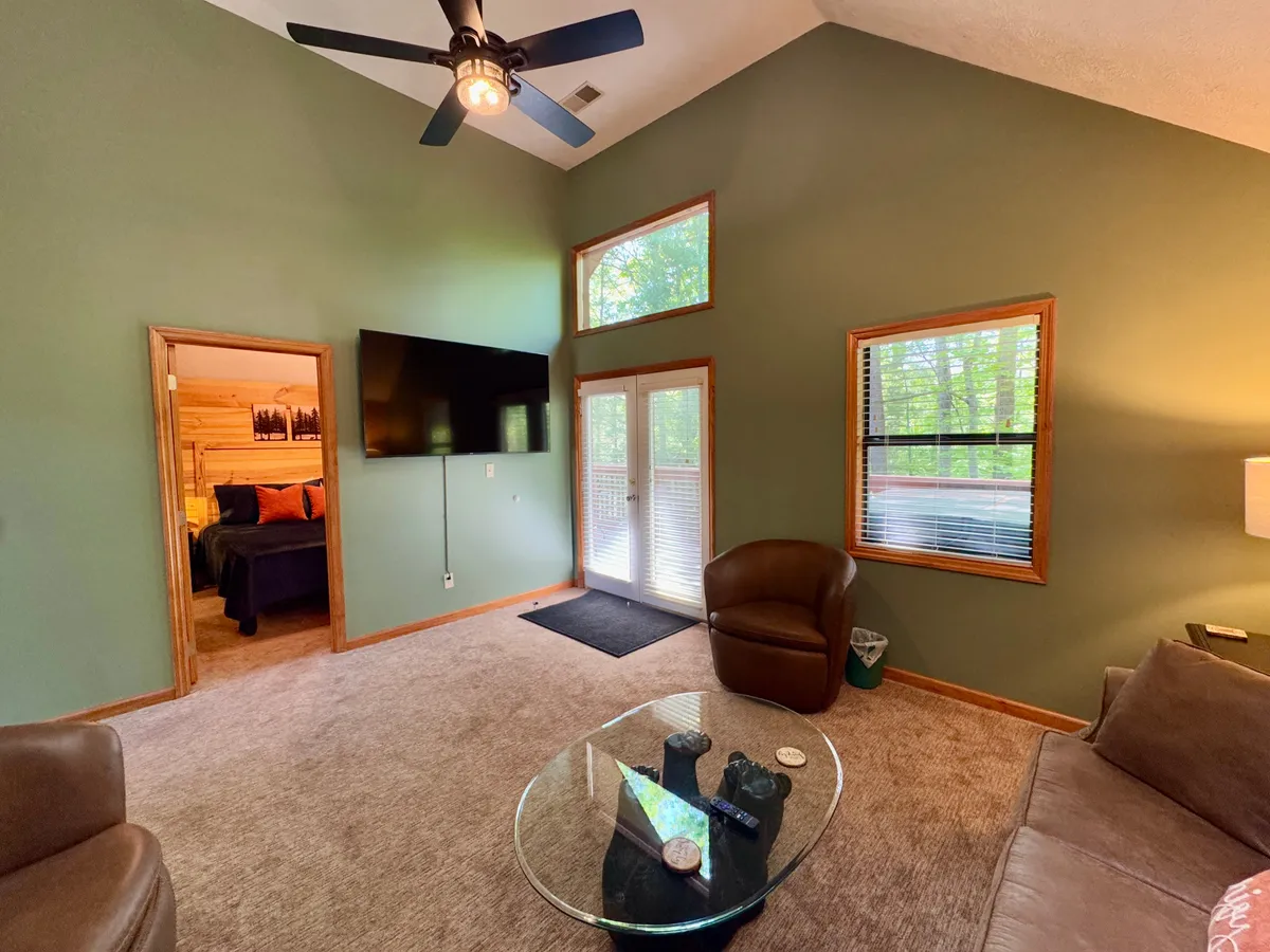 A welcoming living area furnished with comfortable seating, a modern television, a glass coffee table, and expansive windows that offer serene nature views. The setup encourages both social gatherings and cozy movie nights.
