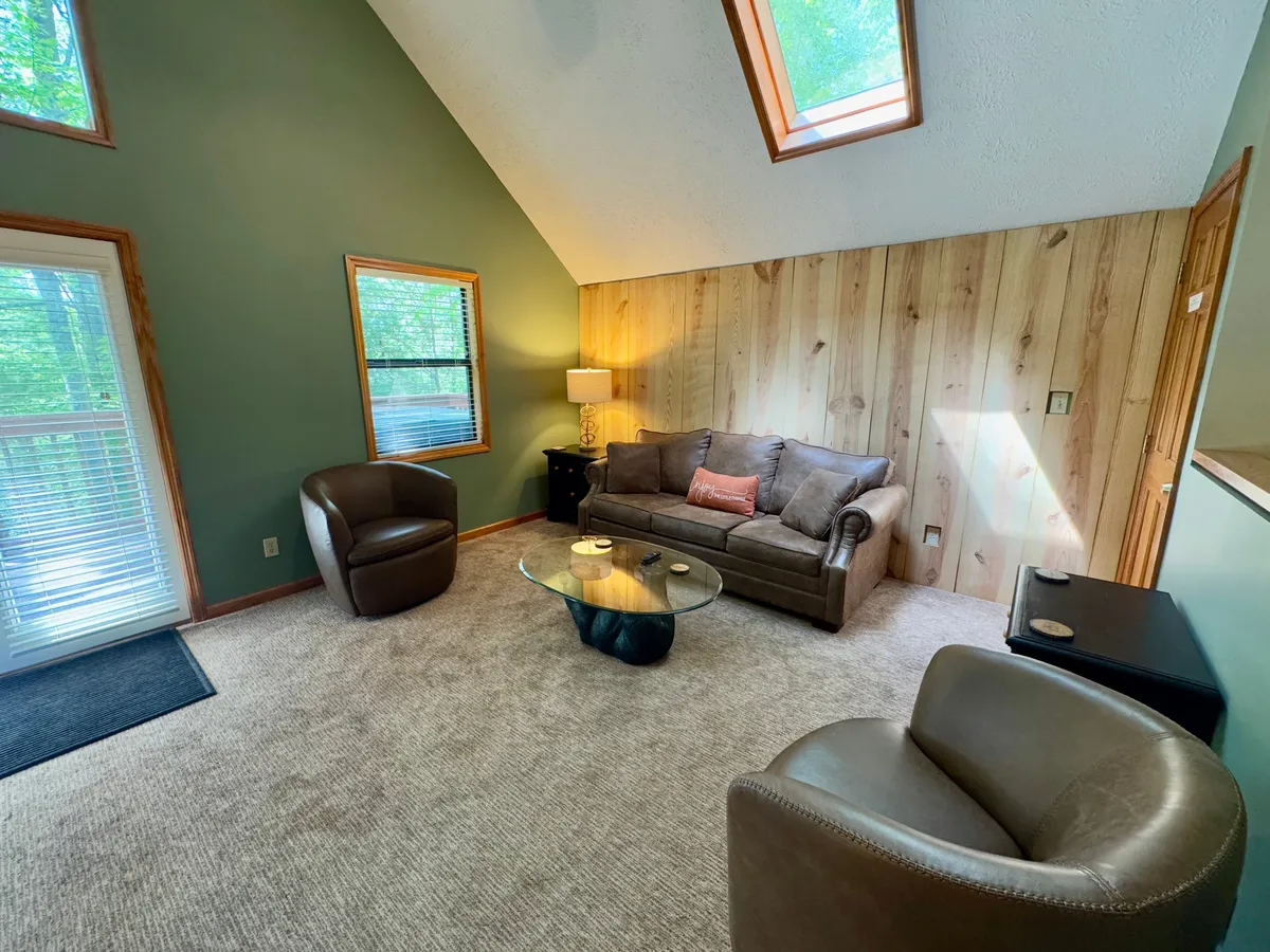 A welcoming living room featuring a comfortable sofa, glass coffee table, armchairs, and wide windows that reveal a glimpse of the outdoors. The arrangement suggests a relaxing space to socialize after a day of adventure, with natural light enhancing the inviting atmosphere.